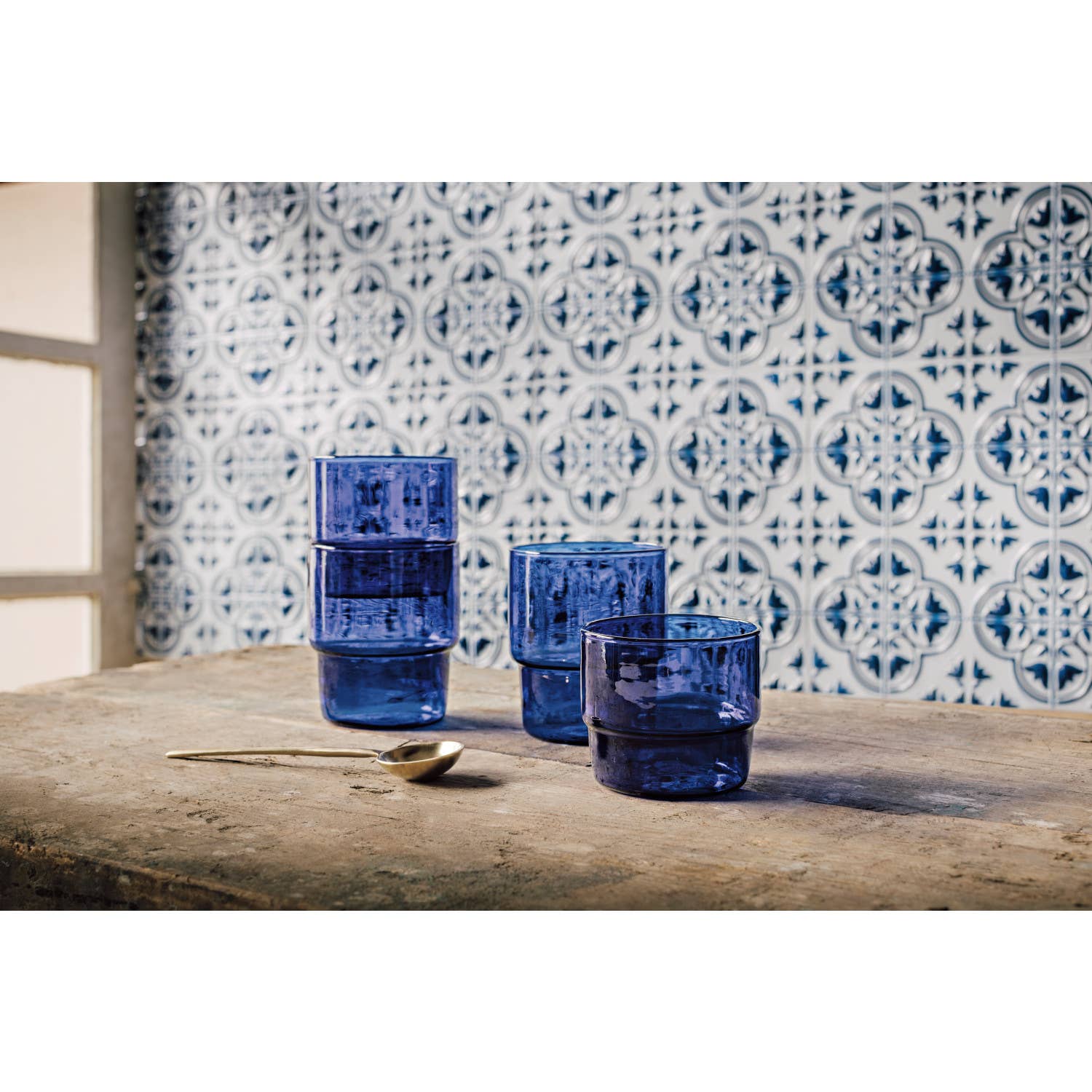 Set of blue glass tumblers on a wooden surface with a patterned tile background