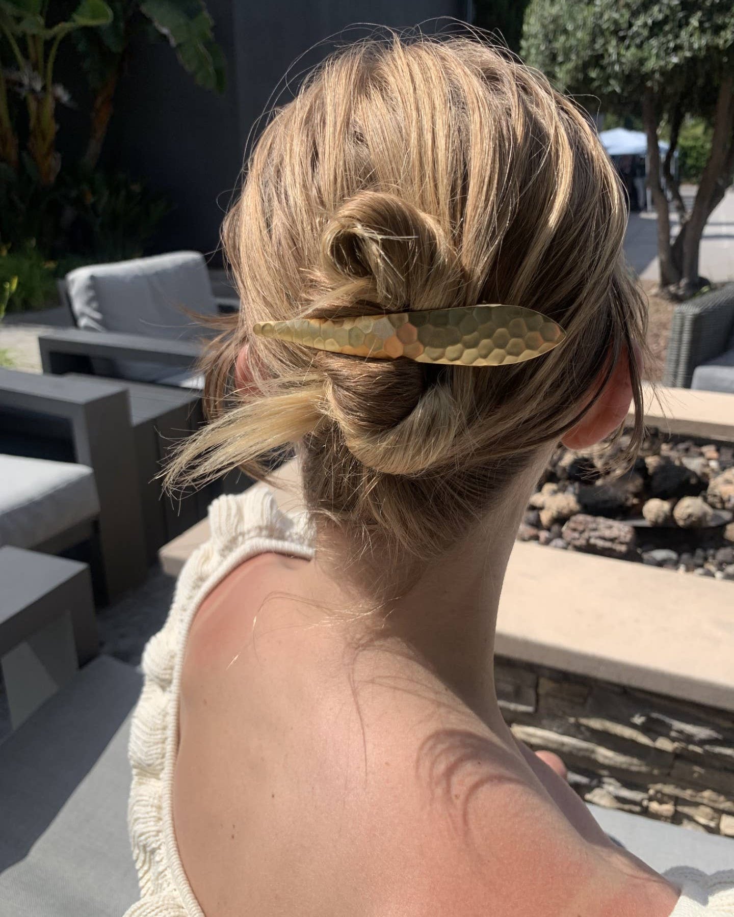 Person with a styled hair bun wearing a gold leaf accessory outdoors.