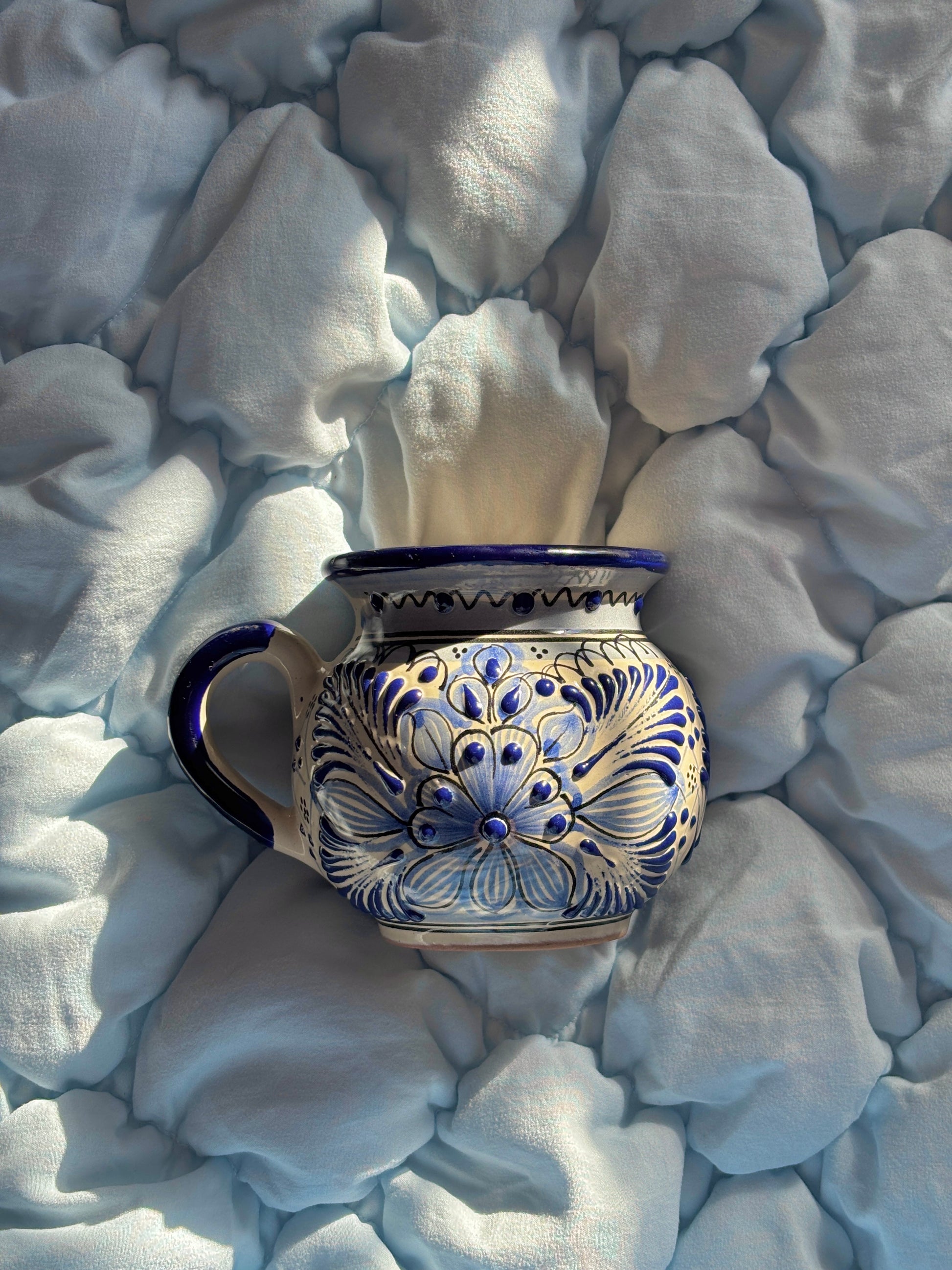 Decorative ceramic mug with blue floral patterns on a white fabric background