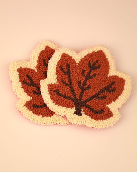 Two leaf-shaped coasters with brown leaves on a beige background
