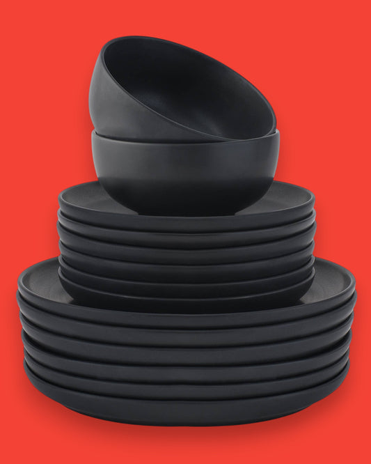 Matte black stoneware dinnerware set with plates and bowls stacked on a table.