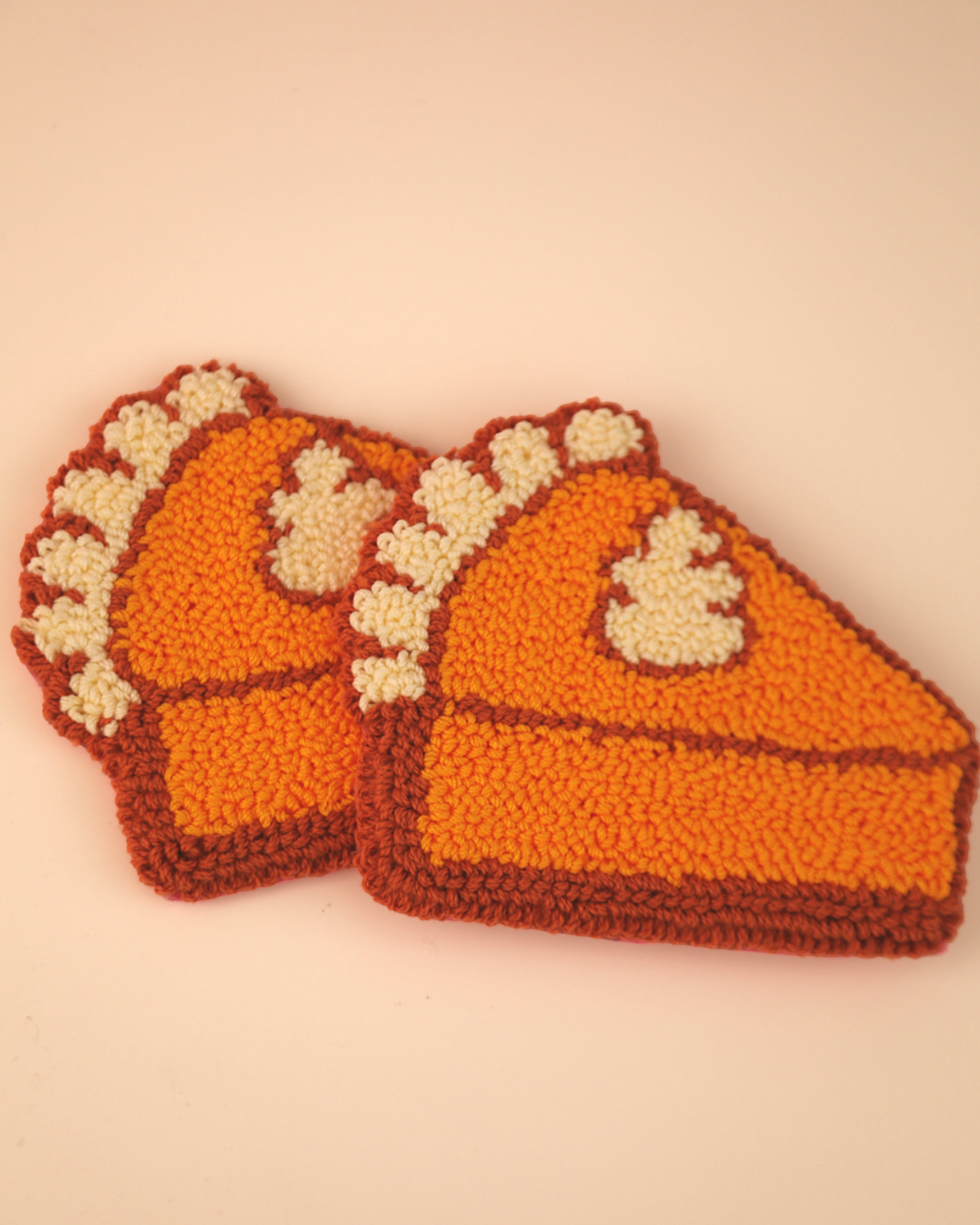 Two knitted pumpkin pie coasters on a beige background