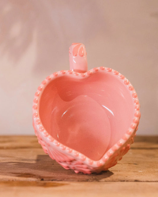 Pink glass heart-shaped container on a wooden surface.